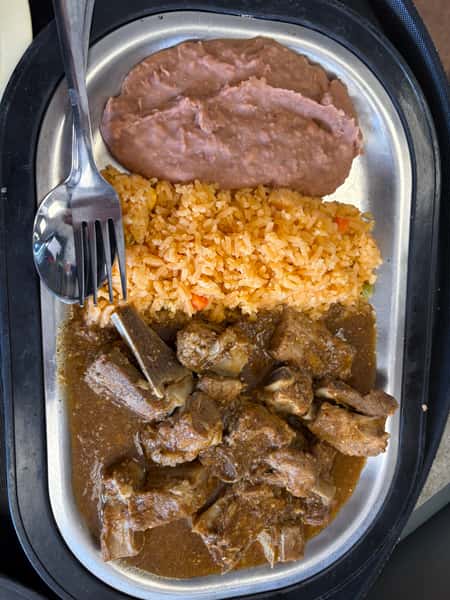 Mexican-style plate with refried beans, seasoned rice, and tender beef ribs in a rich brown sauce, served on a metal tray.