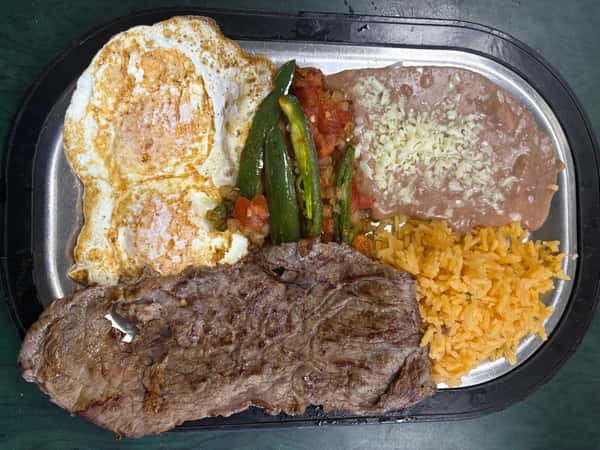 Grilled steak platter with two sunny-side-up eggs, refried beans topped with cheese, Mexican rice, and sautéed jalapeños with salsa.