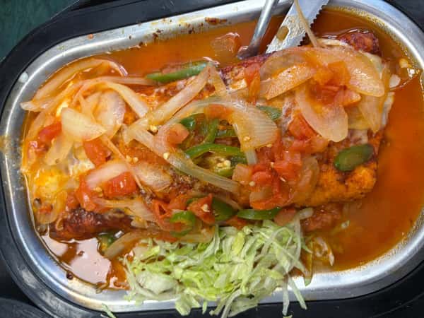 Smothered burrito topped with sautéed onions, tomatoes, and jalapeños in a red sauce, served with a side of shredded lettuce.