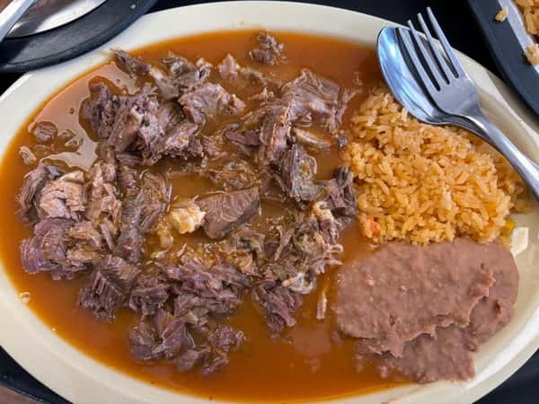 Birria plate featuring tender shredded beef in a rich broth, served with Mexican rice and refried beans on a beige oval plate.
