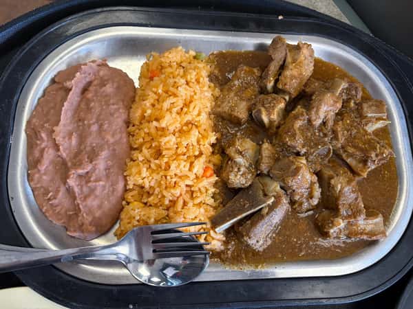 Mexican-style plate with refried beans, seasoned rice, and tender beef ribs in a rich brown sauce, served on a metal tray.