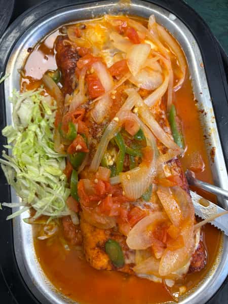 Smothered burrito topped with sautéed onions, tomatoes, and jalapeños in a red sauce, served with a side of shredded lettuce.