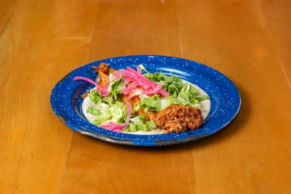 Side view of a pulled pork taco topped with lettuce, pink pickled onions, and cilantro.