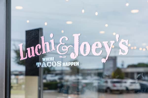 Luchi & Joey's logo on the front window with reflections of the parking area.