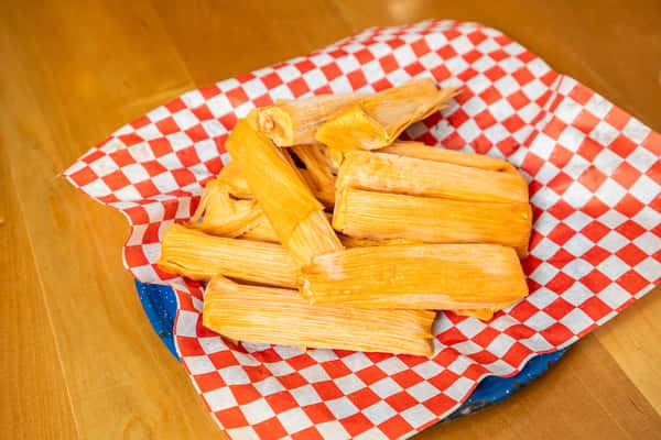 Golden tamales stacked in a basket lined with red-and-white checked paper.