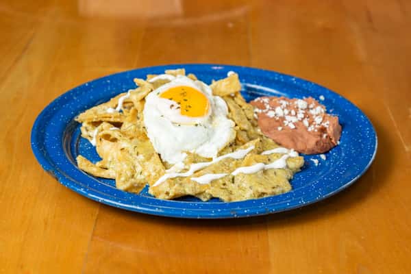 Overhead view of chilaquiles topped with a fried egg and served with refried beans on a blue plate.
