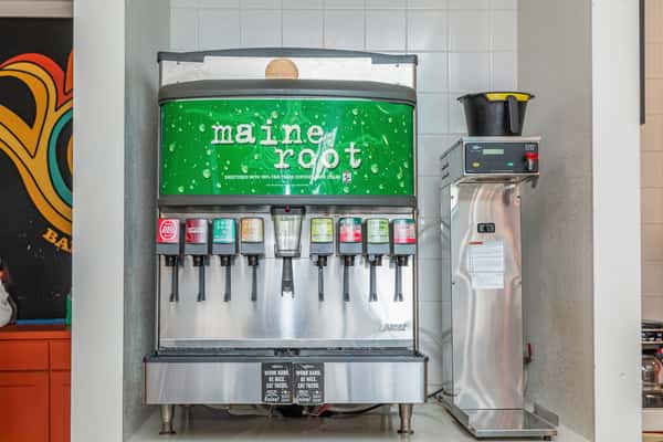Self-service fountain drink machine with multiple dispensers beside a countertop appliance.