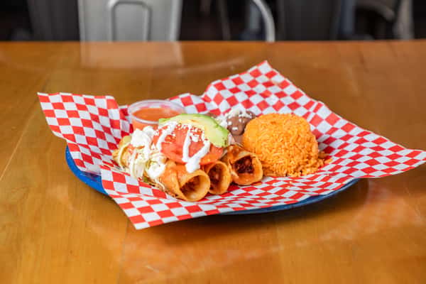 Angled view of chicken flautas with shredded lettuce, rice, refried beans, and salsa on a blue plate.
