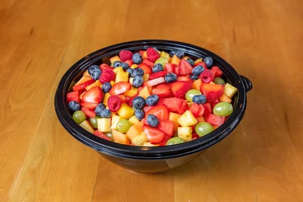 Angled view of a large black bowl filled with colorful berries, grapes, and chopped fruit.