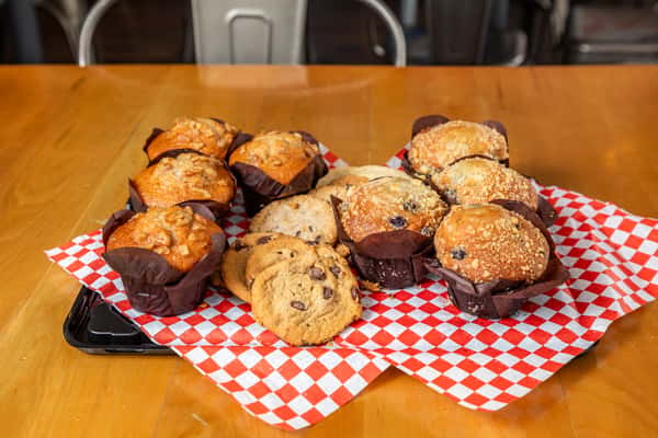 Muffins and cookies arranged on a paper-lined black tray on a wooden table.