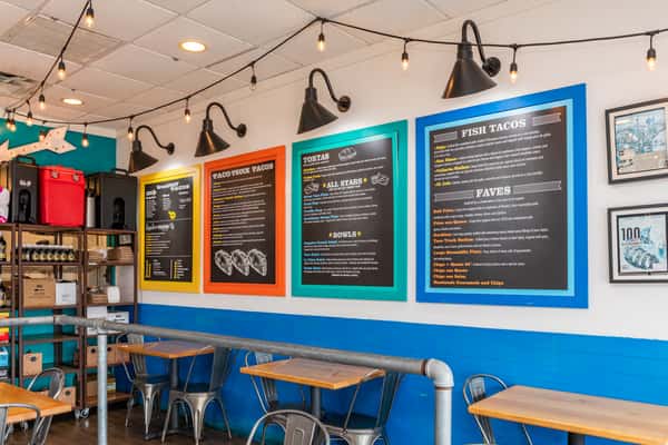 Colorfully framed chalkboards above wooden tables and metal chairs along a blue-and-white wall.