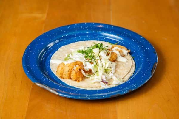 Fish taco topped with shredded cabbage, white sauce, and cilantro, viewed at an angle on a blue plate.