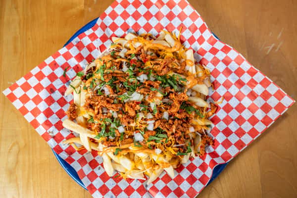 Angled view of loaded fries topped with meat, sauce, and cilantro on checkered paper.