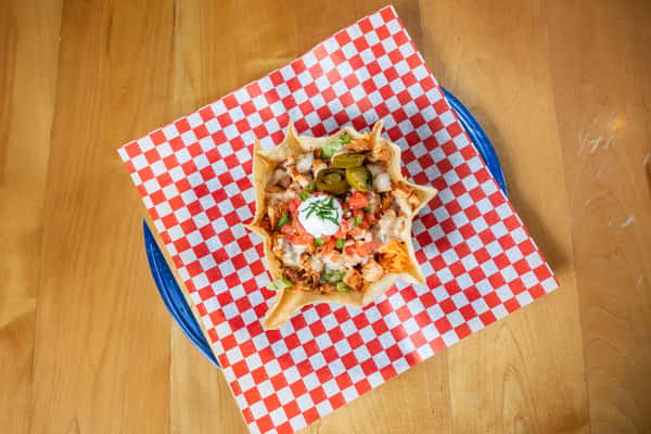 Overhead view of a tortilla bowl filled with lettuce, tomatoes, cheese, and a dollop of sour cream.