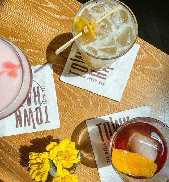 Photo of 3 colorful drinks on a wooden table with branded Town Hall cocktail napkins