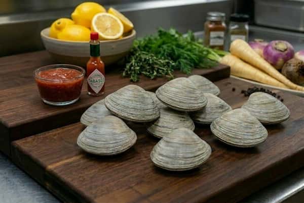 Cherrystones on a display board with cocktail sauce, tabasco, lemons. carrots, and greens