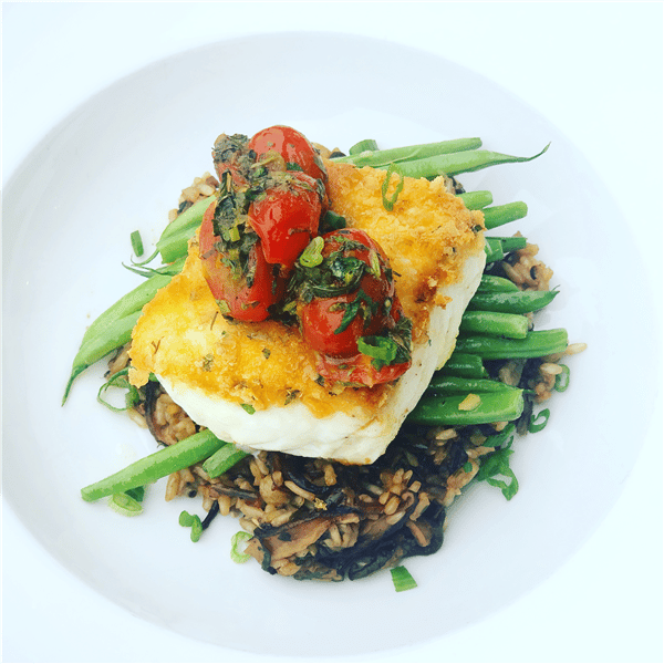 slice of grilled fish on a bed of string beans with tomatoes on top