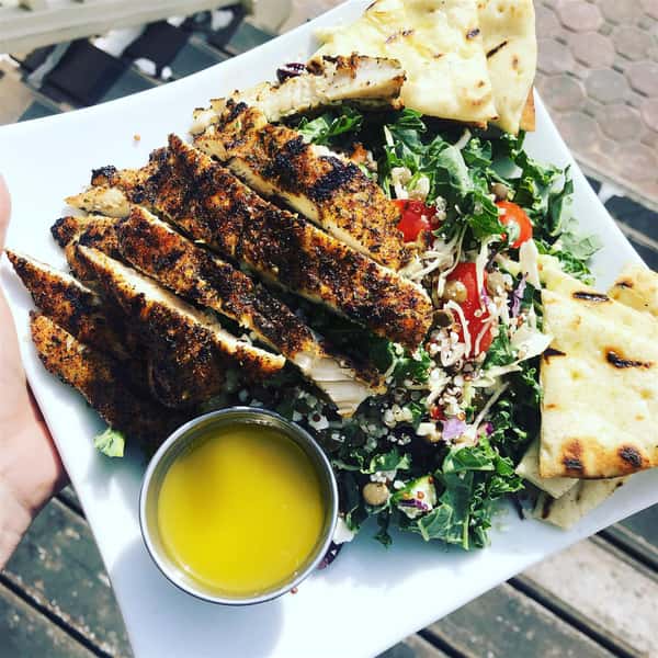 a salad with white dressing, tomatoes, flatbread and grilled chicken