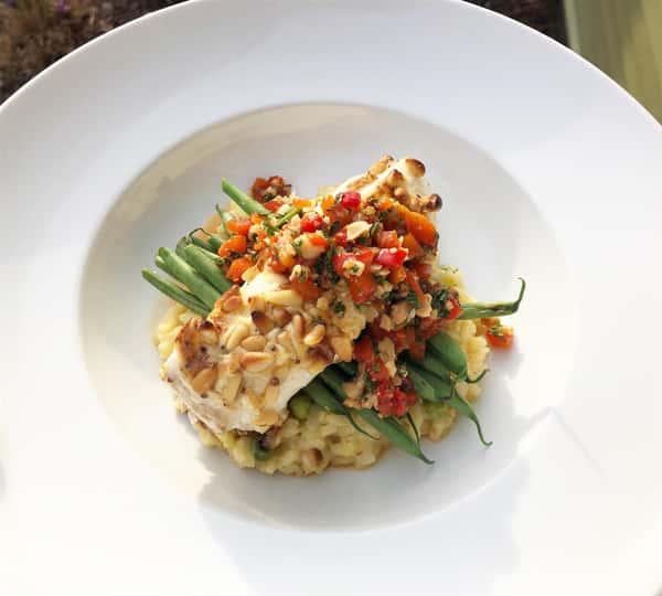 a piece of fish on a bed of paella and string beans with red peppers on top