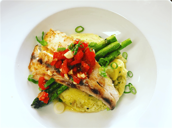 a piece of fish on a bed of paella and asparagus with red peppers on top