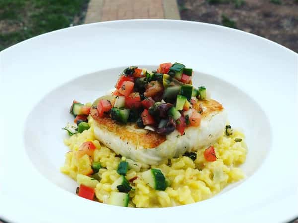 grilled fish on paella with chopped veggies on top