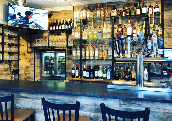view of the bar with bar stools and many bottles of liquor with a tv mounted on the wall