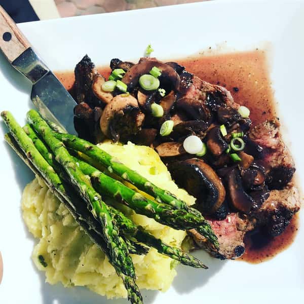 Steak topped with mushrooms and a side of mashed potatoes