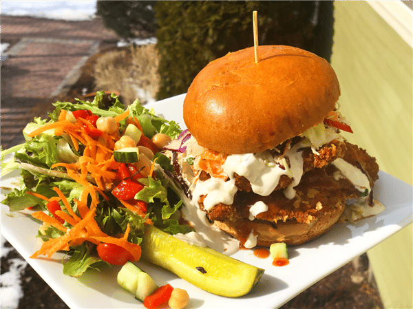 a chicken burger with cream sauce with a side of mixed veggies and a pickle