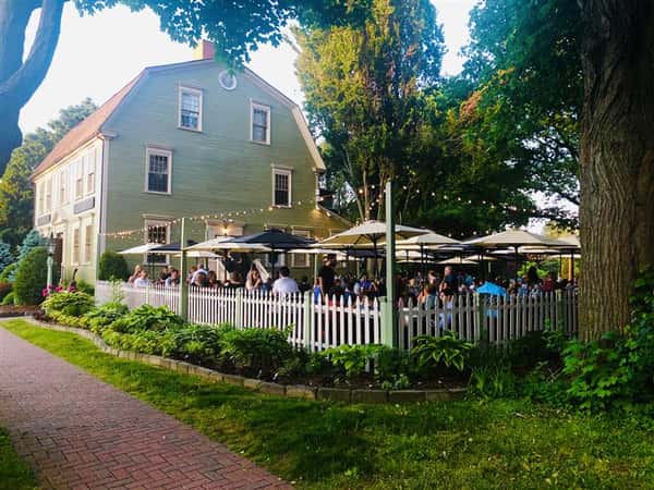 a view of the outdoor seating area from the sidewalk that shows outdoor lights and many people under the umbrellas
