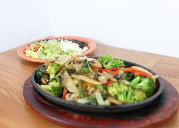 Mixed vegetable fajitas on a skillet with a side of lettuce, tomatoes, beans and rice