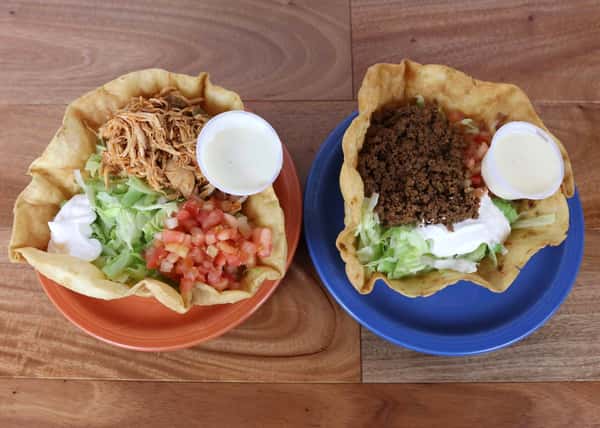 Two taco salad bowls side by side filled with pulled pork and beef with lettuce, tomatoes and sour cream