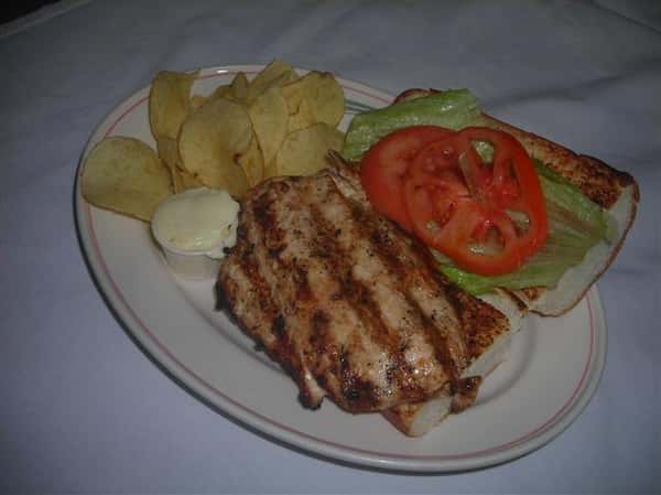 Grilled chicken with a side of Potato chips, Lettuce, and tomatoes. Along with sauce