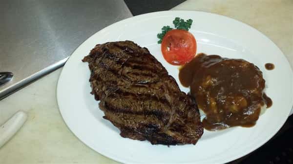 Steak with a side of mashed potatoes, lettuce, and a tomato slice