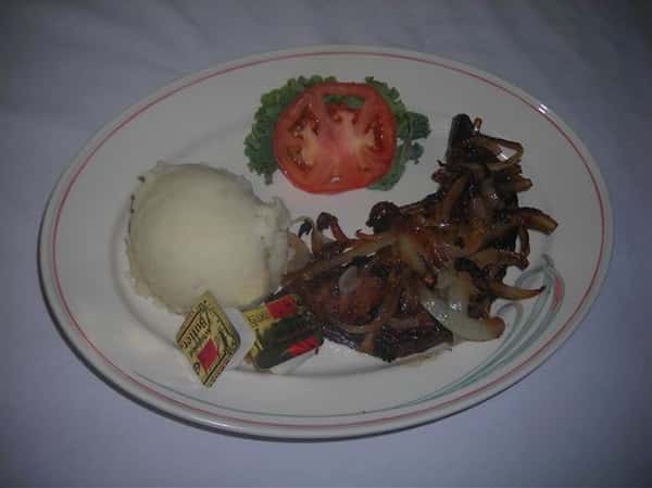 Steak topped with grilled onions with a side of mashed potatoes, lettuce, and tomatoes