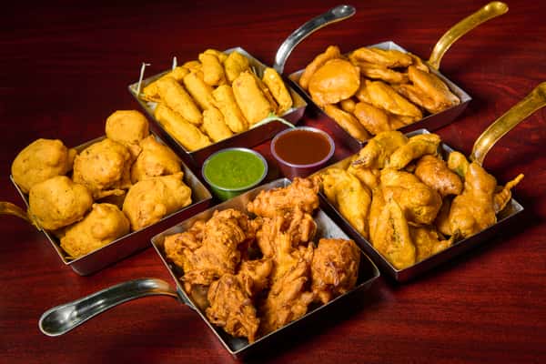 Assorted Indian appetizers platter at Dhaba Express in Parsippany, NJ, featuring pakoras, samosas, and crispy snacks with chutneys in a rustic dhaba-style spread