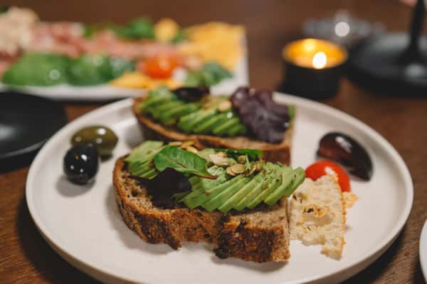 Avocado toast topped with fresh greens and seeds, served on a wooden board