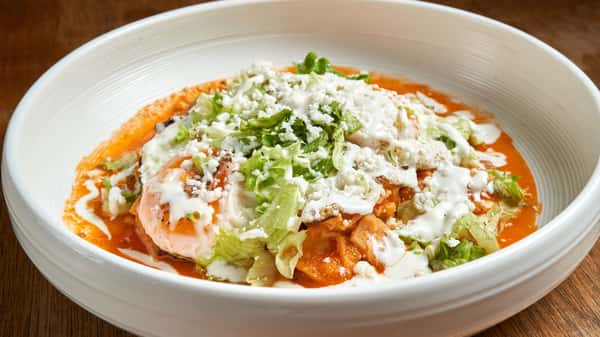 Close-up of traditional chilaquiles topped with fresh lettuce, crumbled cheese, and cream