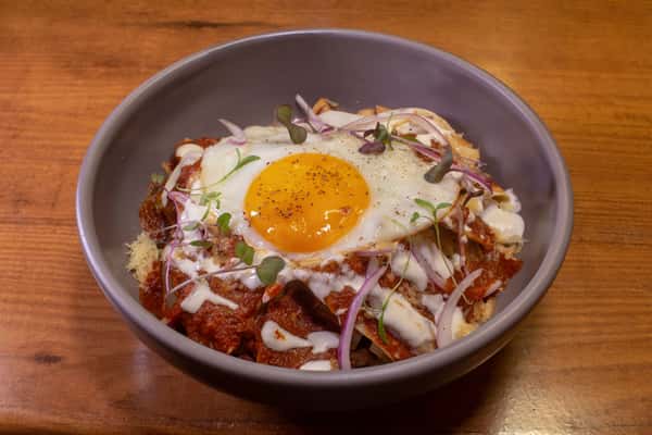 Bowl of chilaquiles topped with a sunny-side-up egg, red salsa, and sliced onions
