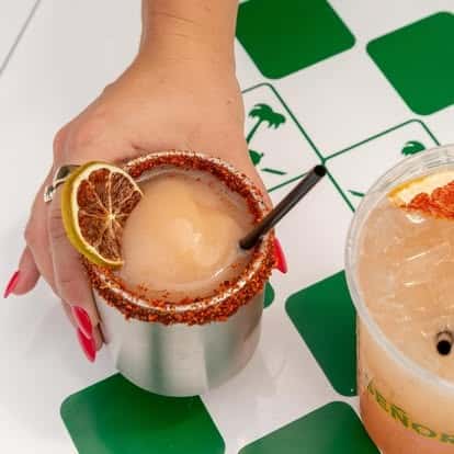 Refreshing Mexican cocktail with chili-salt rim and dried citrus garnish, paired with iced agua fresca—vibrant handcrafted drinks in a trendy taqueria setting.