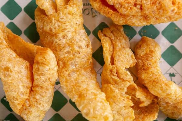 Golden, airy chicharrones with bubbly, crunchy texture served on branded liner—house-made Mexican pork rinds ideal for dipping or sharing.