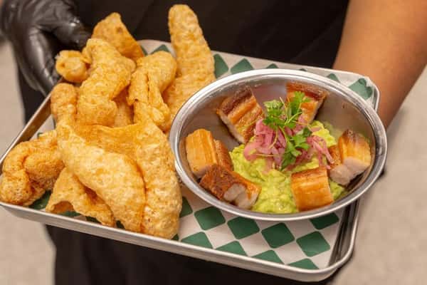 Crispy chicharrones served with thick-cut pork belly over smooth guacamole, topped with pickled onions and cilantro—bold, shareable Mexican appetizer.