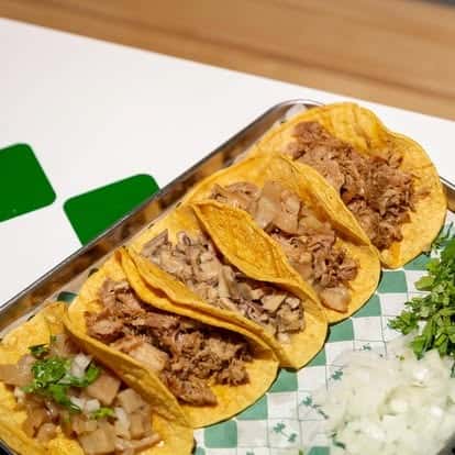 Tray of authentic Mexican street tacos with various seasoned meats, served on warm corn tortillas with chopped onion, cilantro, and fresh lime—classic taqueria favorites.