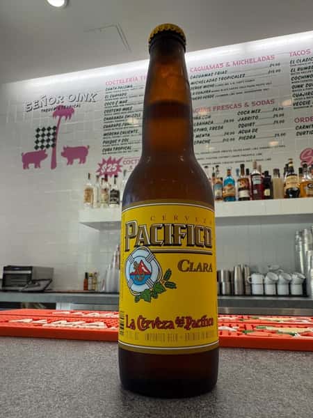 Chilled Pacifico Clara cerveza bottle on the bar counter with full cocktail menu backdrop—classic Mexican lager perfect with tacos and bold street food flavors.