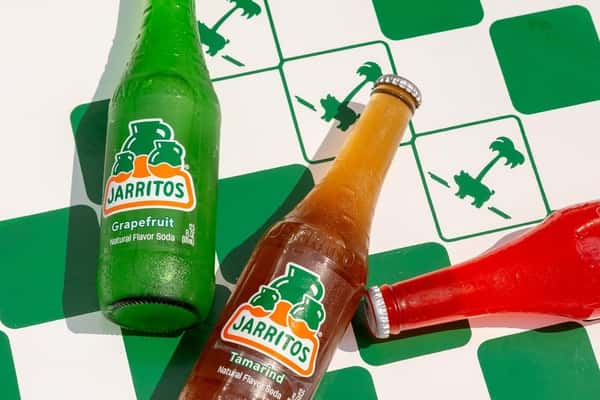 Assorted Jarritos natural fruit sodas including grapefruit and tamarind, served chilled on a green checkered table—classic Mexican soft drinks perfect for pairing with tacos.