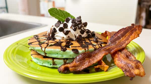 Stack of mint pancakes topped with chocolate chips and served with bacon.