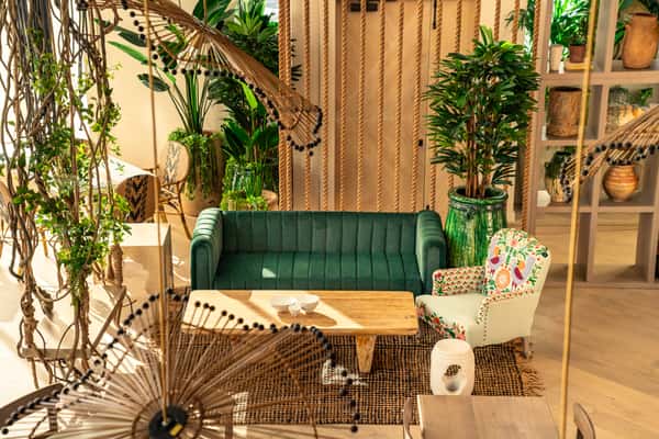 Cozy restaurant booth seating with tropical plants, woven decor, and modern upscale dining atmosphere