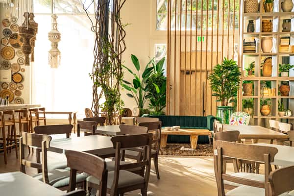 Modern restaurant dining area with natural wood accents, tropical plants, and upscale contemporary styling