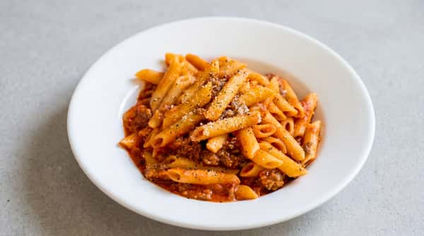 Penne pasta with a meat sauce and sprinkled Parmesan cheese in a white bowl.