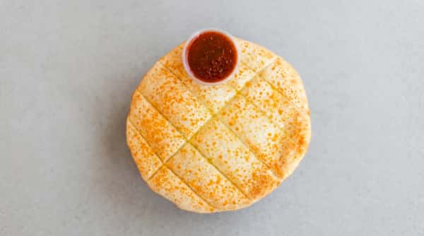 Cheesy breadsticks, cut into squares, with a cup of marinara sauce on a red surface.