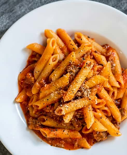 Penne pasta with a meat sauce and sprinkled Parmesan cheese in a white bowl.